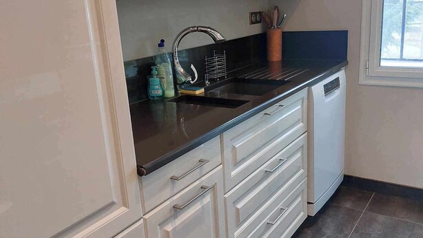 A kitchen with white cabinets, a black countertop, a stainless steel sink, and a dishwasher.