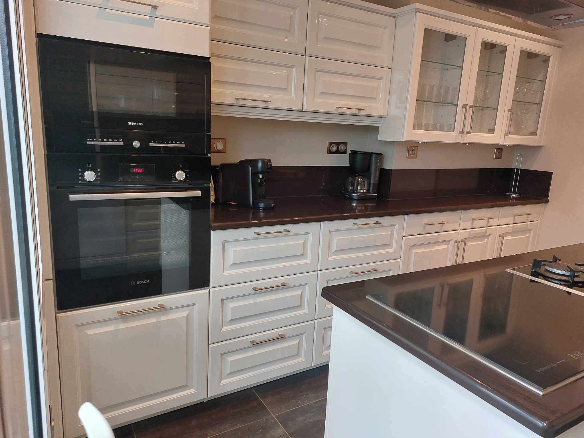A modern kitchen with white cabinetry, a Bosch oven, and a coffee maker.