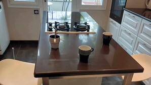 A modern kitchen with a central island, two bar stools, a gas stove, and a view through large windows.