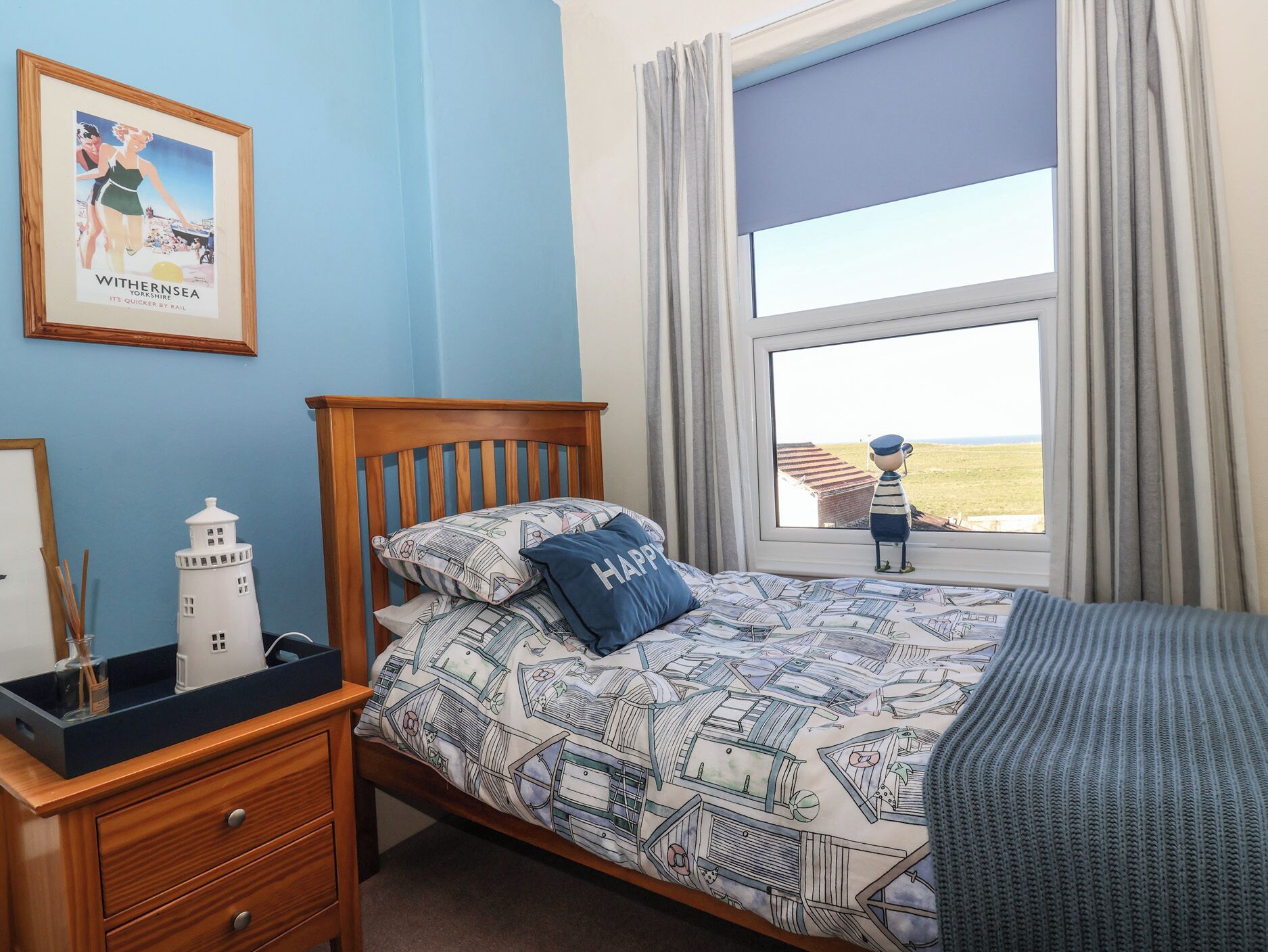 A bedroom with a bed, a nightstand, a lamp, a framed picture, a window with a view, and a small lighthouse model.