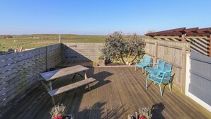 A wooden deck with picnic tables and blue chairs, overlooking a grassy field. - 48 Waxholme Road (Withernsea)
