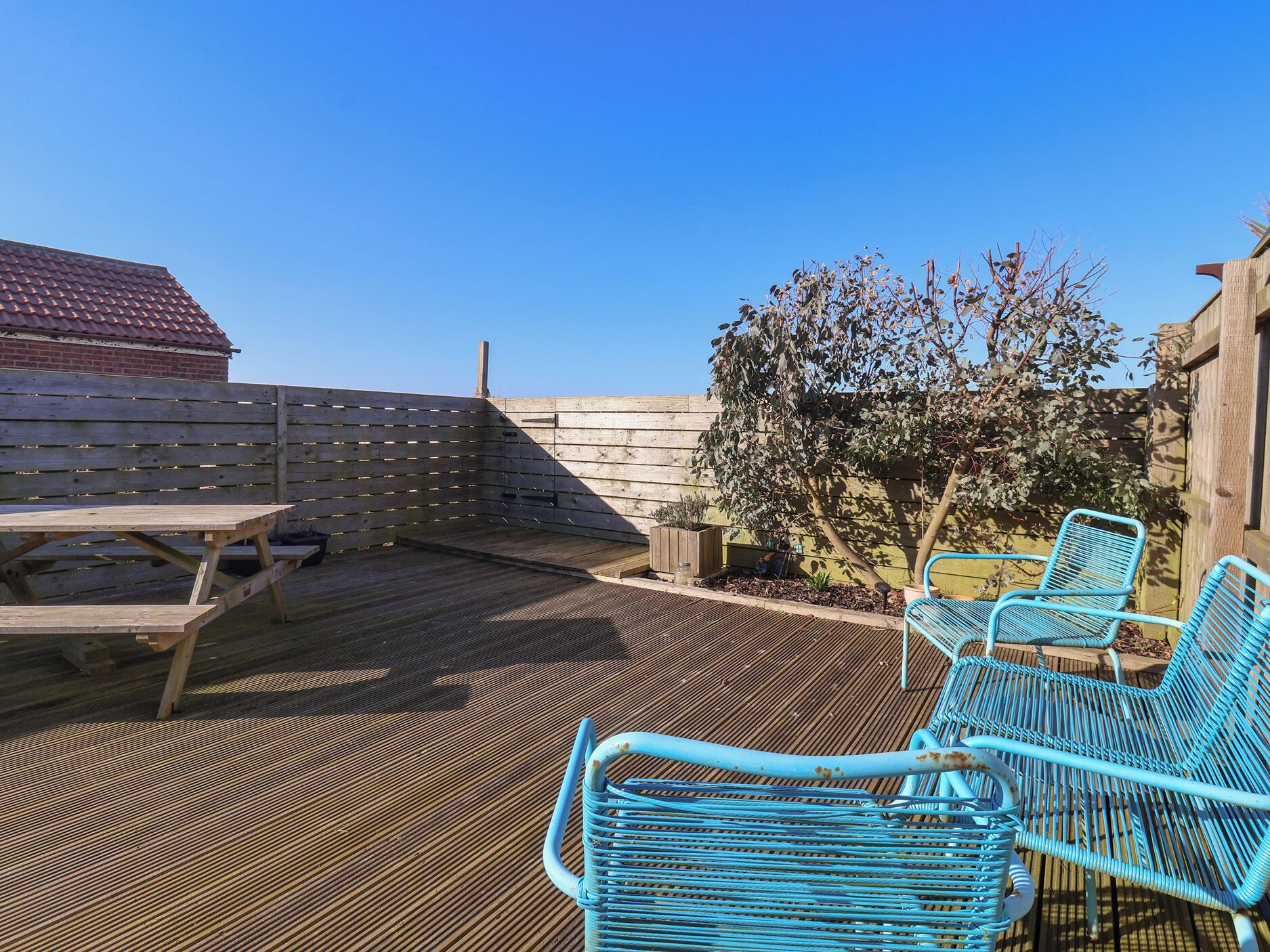 A patio with a wooden deck, a picnic table, and blue metal chairs.