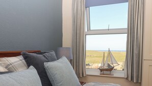 A bedroom with a bed, pillows, a lamp, and a view of a sailboat on the horizon through a window. - 48 Waxholme Road (Withernsea)