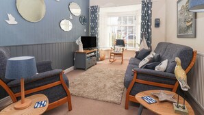 A living room with a sofa, chairs, a TV, and a table with decorative items. - 48 Waxholme Road (Withernsea)