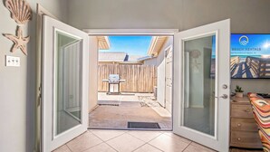 A doorway leading to a backyard with a wooden fence, a grill, and a beach rental sign.