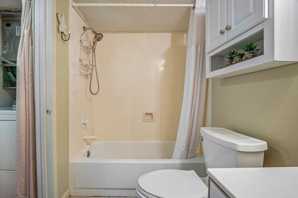Un baño con bañera, inodoro y una estantería con plantas.