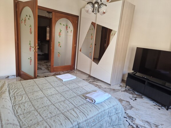 Un dormitorio con cama, televisor, armario con espejos y una puerta que da a otra habitación.