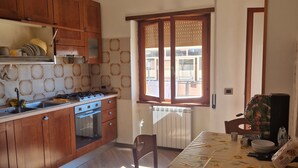 A kitchen with wooden cabinets, a stove, and a dining table with a sunflower tablecloth. - ROYAL HOUSE APPARTMENT DELUXE close to the main services and the sea. (Civitavecchia)
