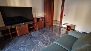 A living room with a flat-screen TV, wooden entertainment unit, and a sofa. - ROYAL HOUSE APPARTMENT DELUXE close to the main services and the sea. (Civitavecchia)