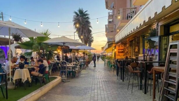 An outdoor dining area with tables and chairs, palm trees, and a brick pathway. - ROYAL HOUSE APPARTMENT DELUXE close to the main services and the sea. (Civitavecchia)