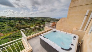 Uma banheira de hidromassagem numa varanda com vista para uma paisagem verde.