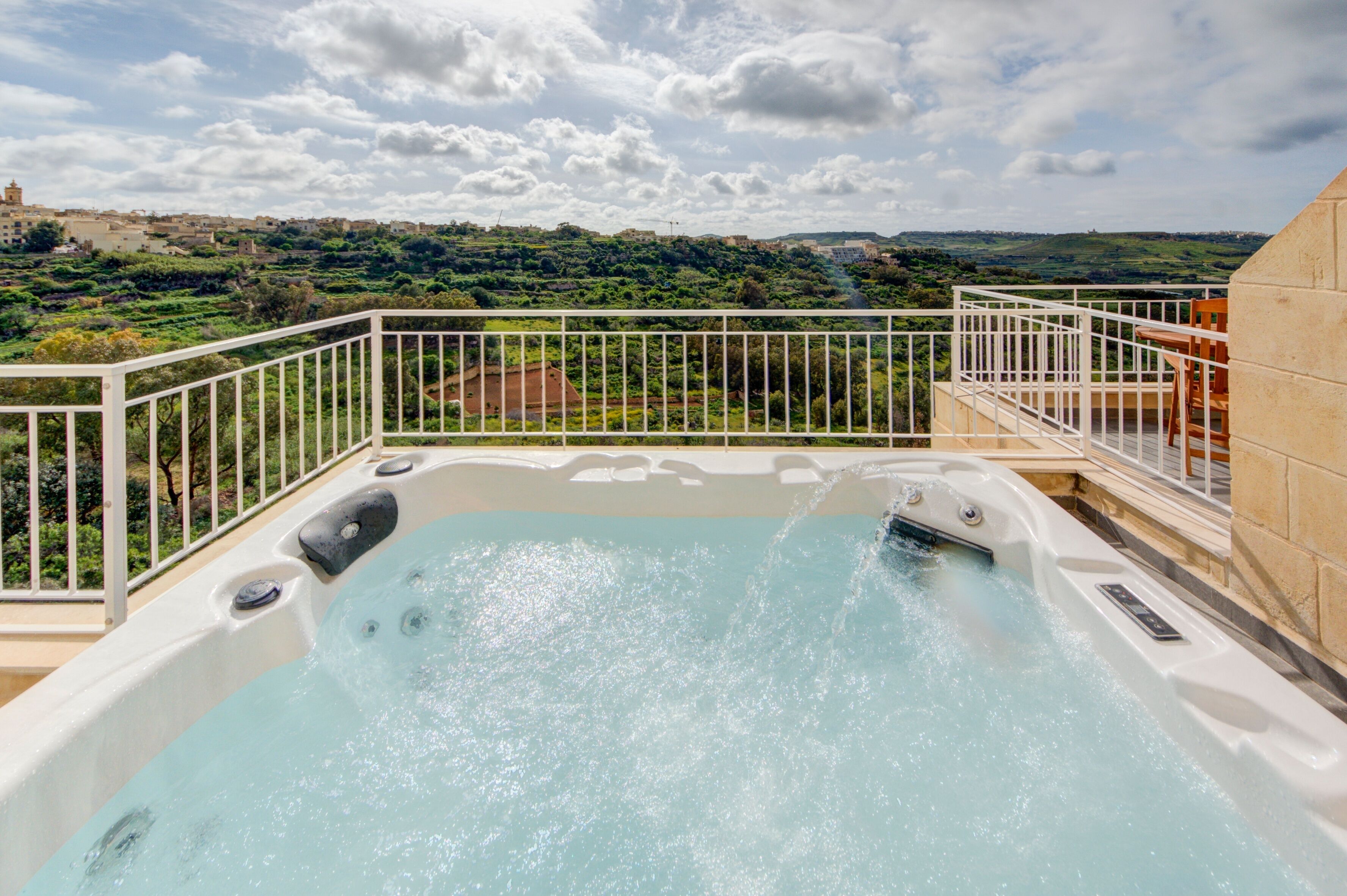 A hot tub on a balcony with a scenic view of a green landscape and buildings in the distance.
