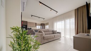 Uma sala de estar moderna com um sofá, uma área de jantar e uma cozinha ao fundo.