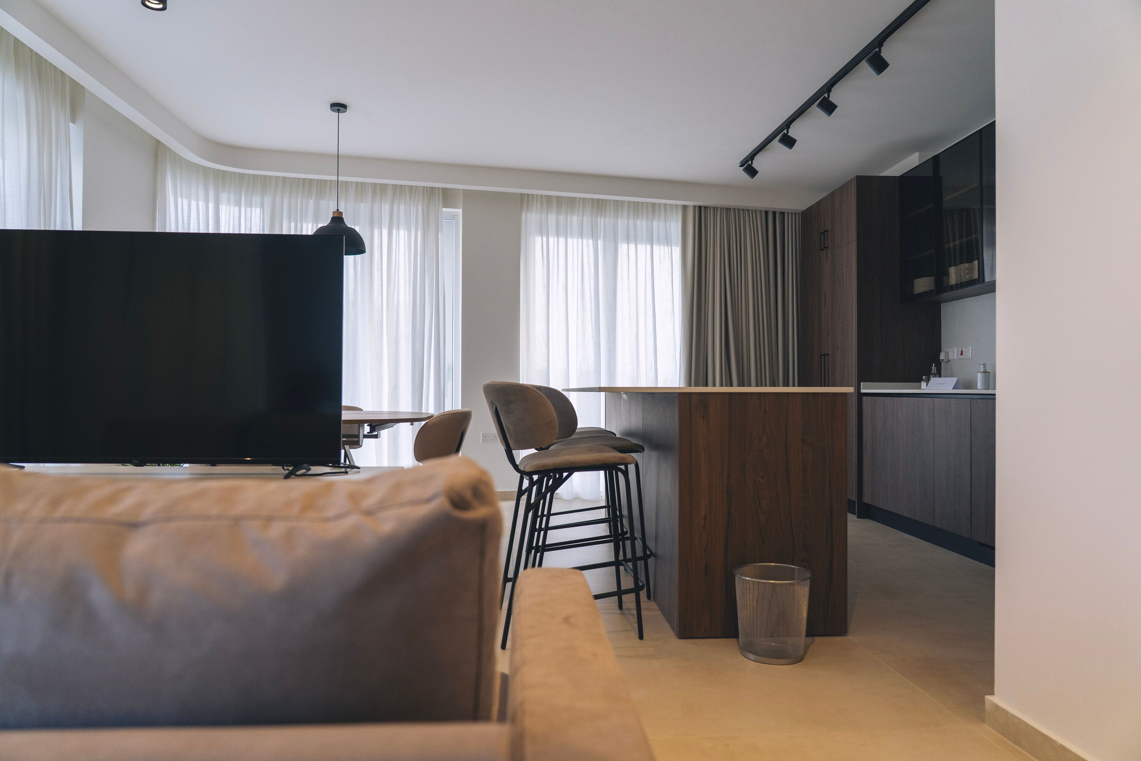 A modern living room with a large flat-screen TV, a sofa, and a dining area with chairs.