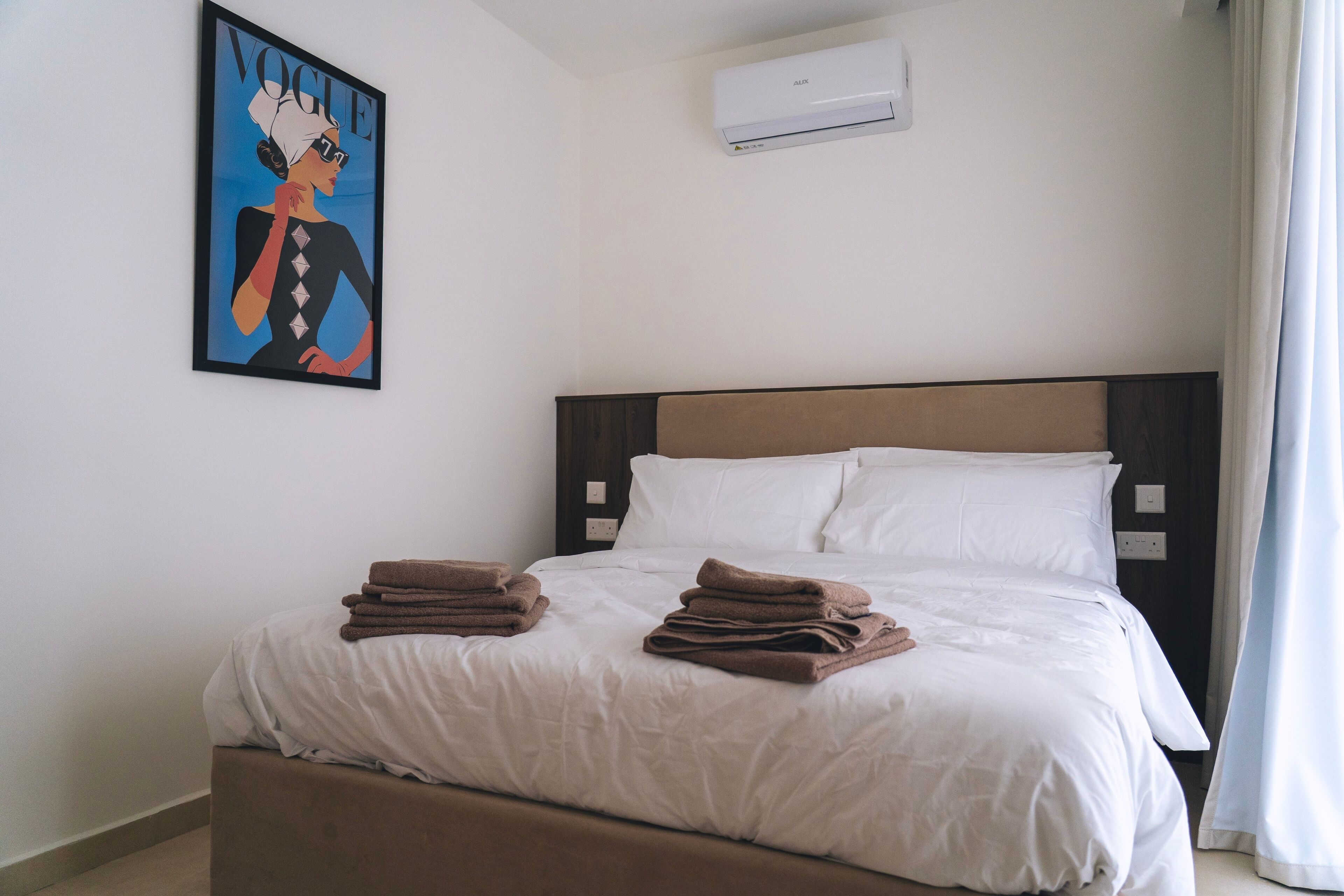 A hotel room with a bed, white bedding, a brown headboard, and a painting on the wall.