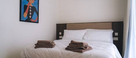 A hotel room with a bed, white bedding, a brown headboard, and a painting on the wall.