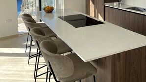 A modern kitchen with a central island, bar stools, and a view of the sea.
