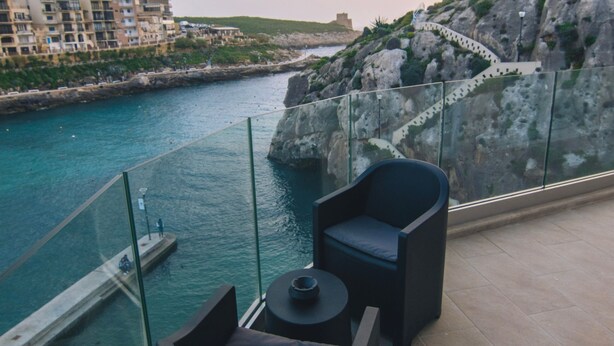 A balcony with a view of a body of water, a chair, and a small table.