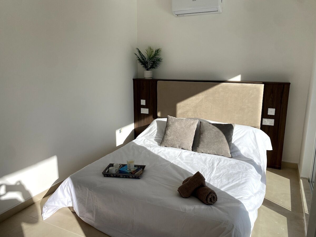 A neatly made bed with white linens, a tray with a book and cups, and a brown towel on the side.
