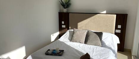 A neatly made bed with white linens, a tray with a book and cups, and a brown towel on the side.
