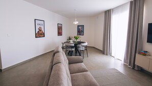 Een moderne woonkamer met een bank, een eettafel met stoelen en een tv op een standaard.