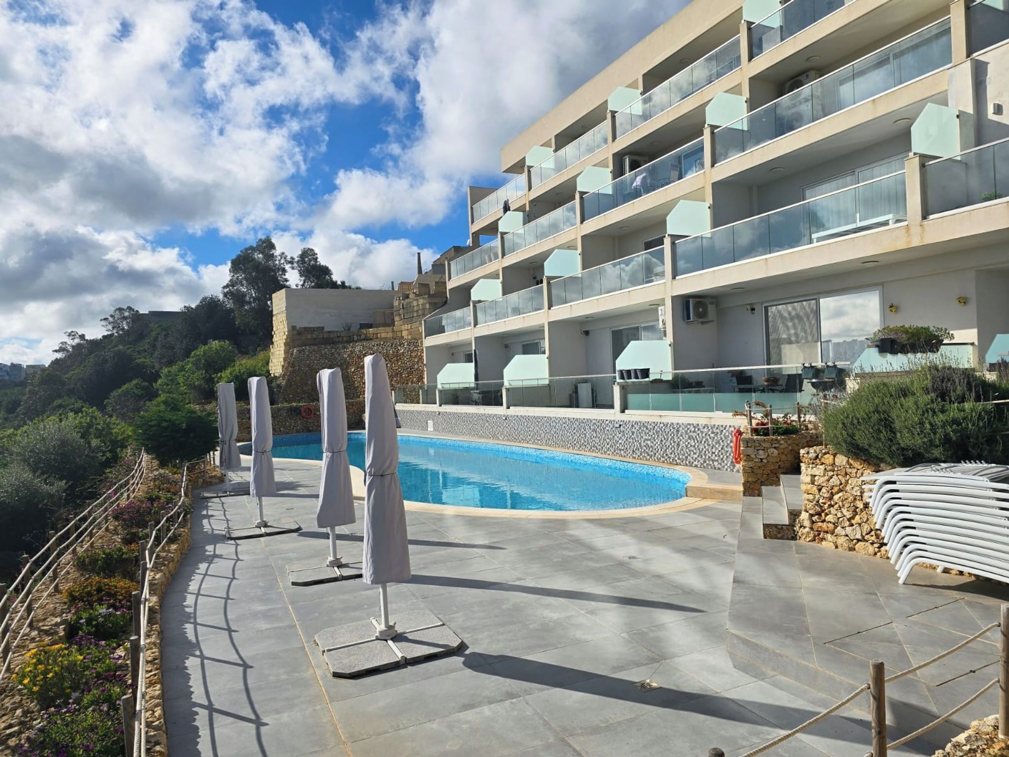 A modern hotel with a swimming pool, outdoor seating, and a view of the surrounding landscape.