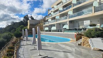 A modern hotel with a swimming pool, outdoor seating, and a view of the surrounding landscape.
