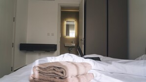 Une chambre d’hôtel avec un lit, une serviette pliée, un bureau avec un ordinateur portable, un miroir et une porte donnant sur une salle de bain.