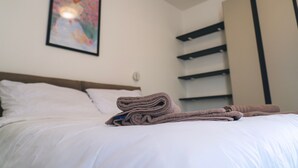 Een net opgemaakt bed met opgevouwen handdoeken, een ingelijst foto aan de muur en een kledingkast met meerdere planken.