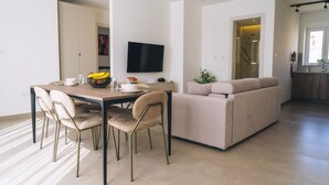 Een moderne woonkamer met een bank, eettafel, stoelen en een flatscreen televisie.