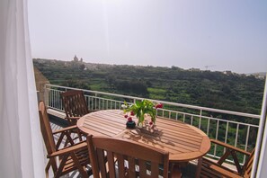 Ein Holztisch und -stühle auf einem Balkon mit Blick auf eine grüne Landschaft und entfernte Gebäude.
