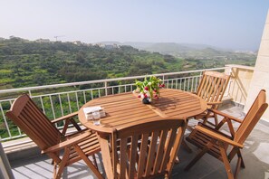 Ein Holztisch und Stühle auf einem Balkon mit Blick auf eine grüne Landschaft.