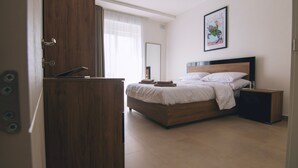 A bedroom with a wooden bed, a bedside table, a mirror, and a door. - The Valley Collection - Suite A10 (Ix-Xagħra)