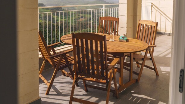 A balcony with a round wooden table and chairs, a view of the countryside, and a white railing. - The Valley Collection - Suite A10 (Ix-Xagħra)