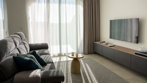 A modern living room with a sofa, a coffee table, a flat-screen TV, and a large window with curtains. - The Valley Collection - Suite B11 (Ix-Xagħra)