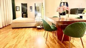 Ein modernes Wohnzimmer mit einer Couch, einem Esstisch mit Stühlen, einer Küchenzeile inklusive Mikrowelle und einem großen Spiegel.