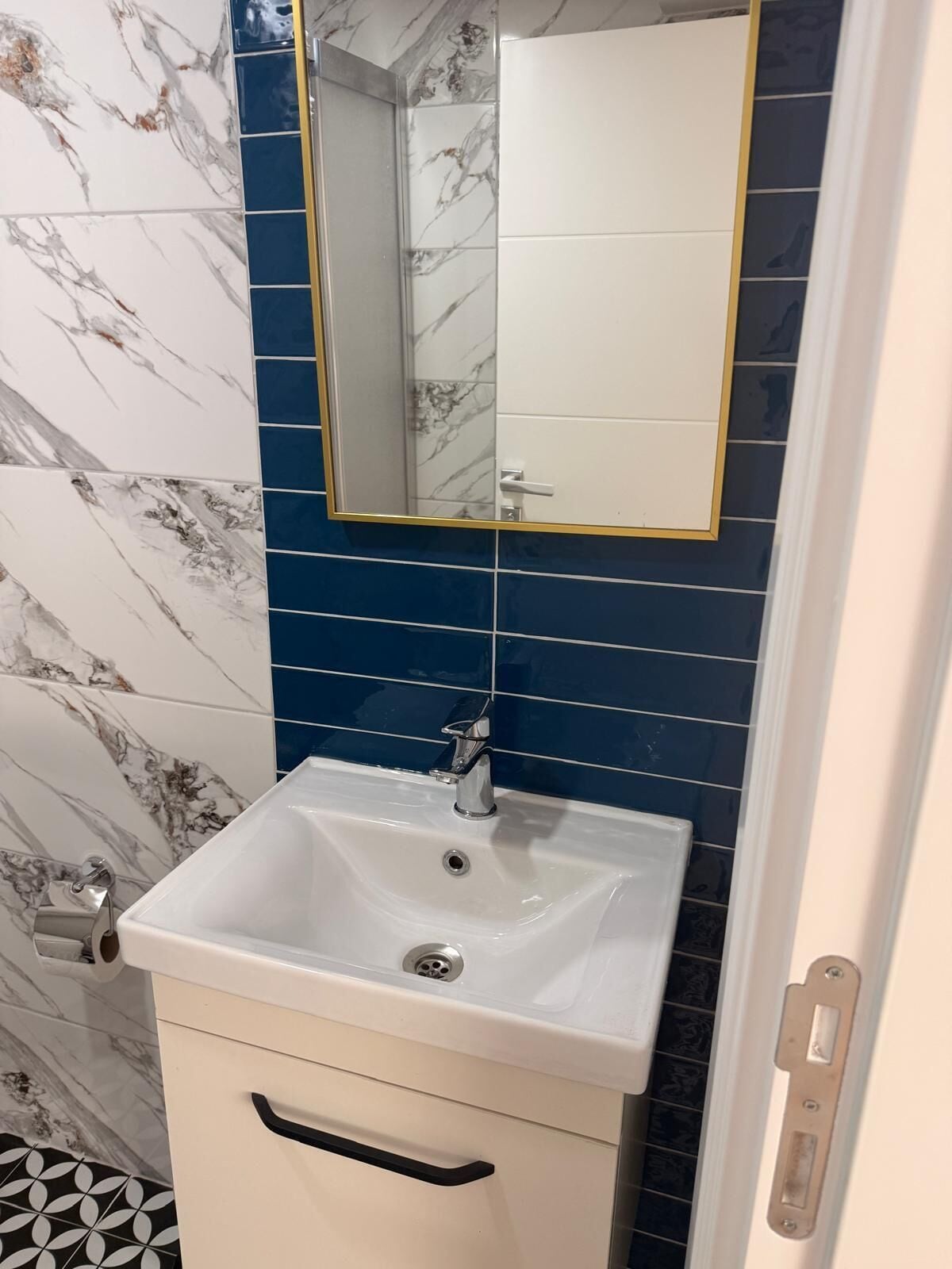 A bathroom with a white sink, a mirror with a gold frame, and blue and white marble tiles.