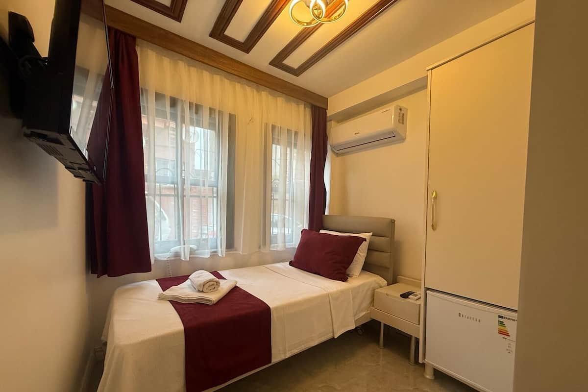 A hotel room with a single bed, a wardrobe, an air conditioning unit, and a television mounted on the wall.