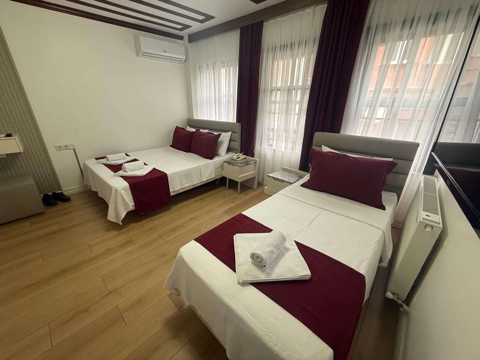 Une chambre d’hôtel avec deux lits, un bureau, une chaise, un appareil de climatisation et une fenêtre avec des rideaux.