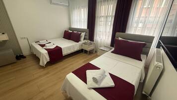 Une chambre d’hôtel avec deux lits, un bureau, une chaise, un appareil de climatisation et une fenêtre avec des rideaux.