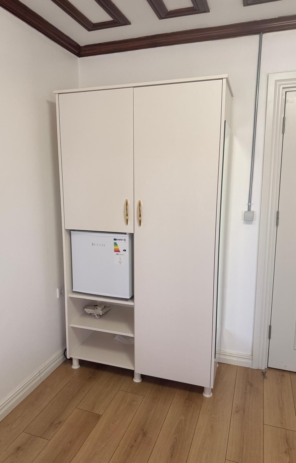 A white wardrobe with a built-in energy monitor, a door, and a wooden floor.