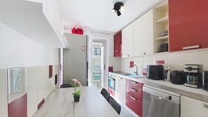 A modern kitchen with white and red cabinetry, a dining table with chairs, a coffee maker, and a dishwasher. - N&J - CLEA - Terrace - Central (Niza)