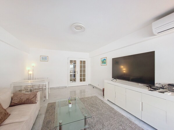 A modern living room with a glass coffee table, a sofa, a TV, and a white cabinet. - N&J - CLEA - Terrace - Central (Niza)