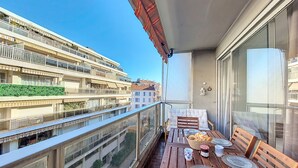 A balcony with a wooden table set for dining, a wicker basket with bread, and a view of a multi-story building with balconies. - N&J - CLEA - Terrace - Central (Niza)
