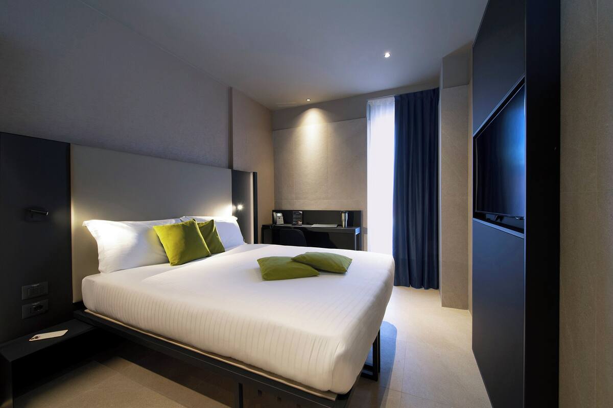 Una habitación de hotel moderna con una cama grande, un escritorio, un televisor de pantalla plana y un baño con ducha e inodoro.