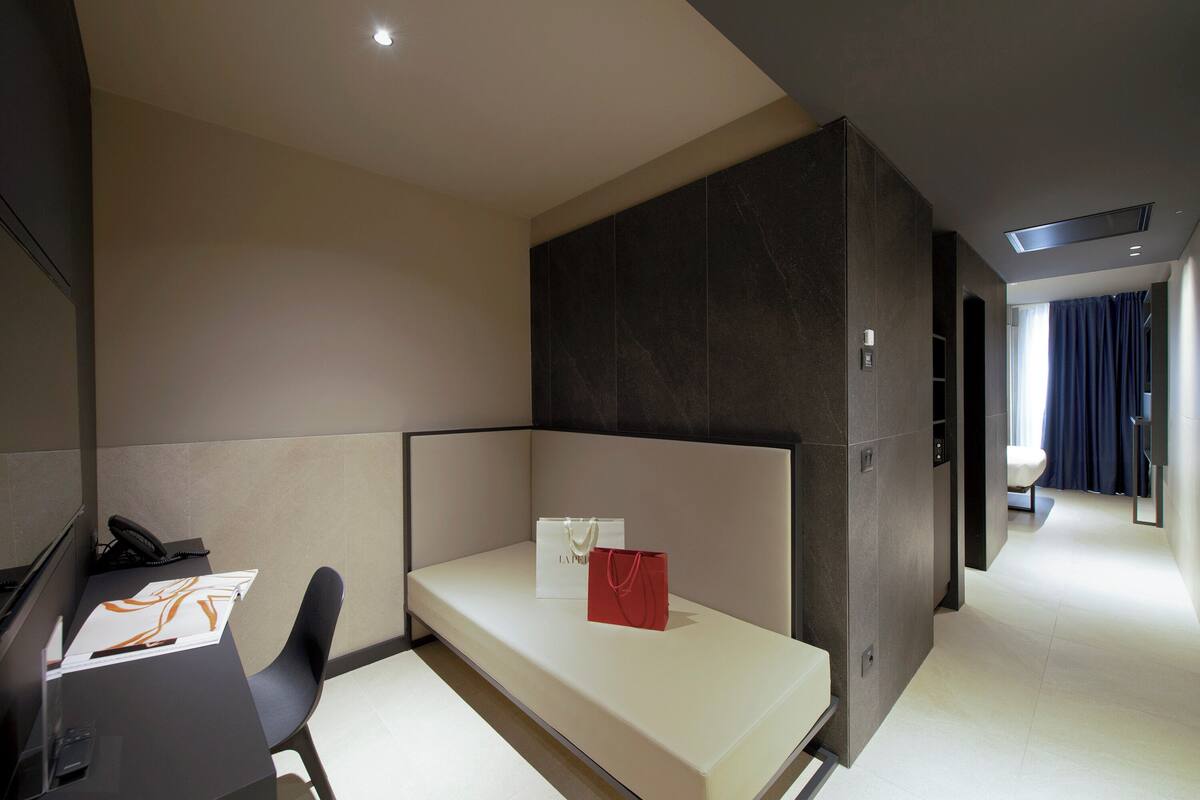 Una habitación de hotel moderna con escritorio, silla y una cama pequeña.