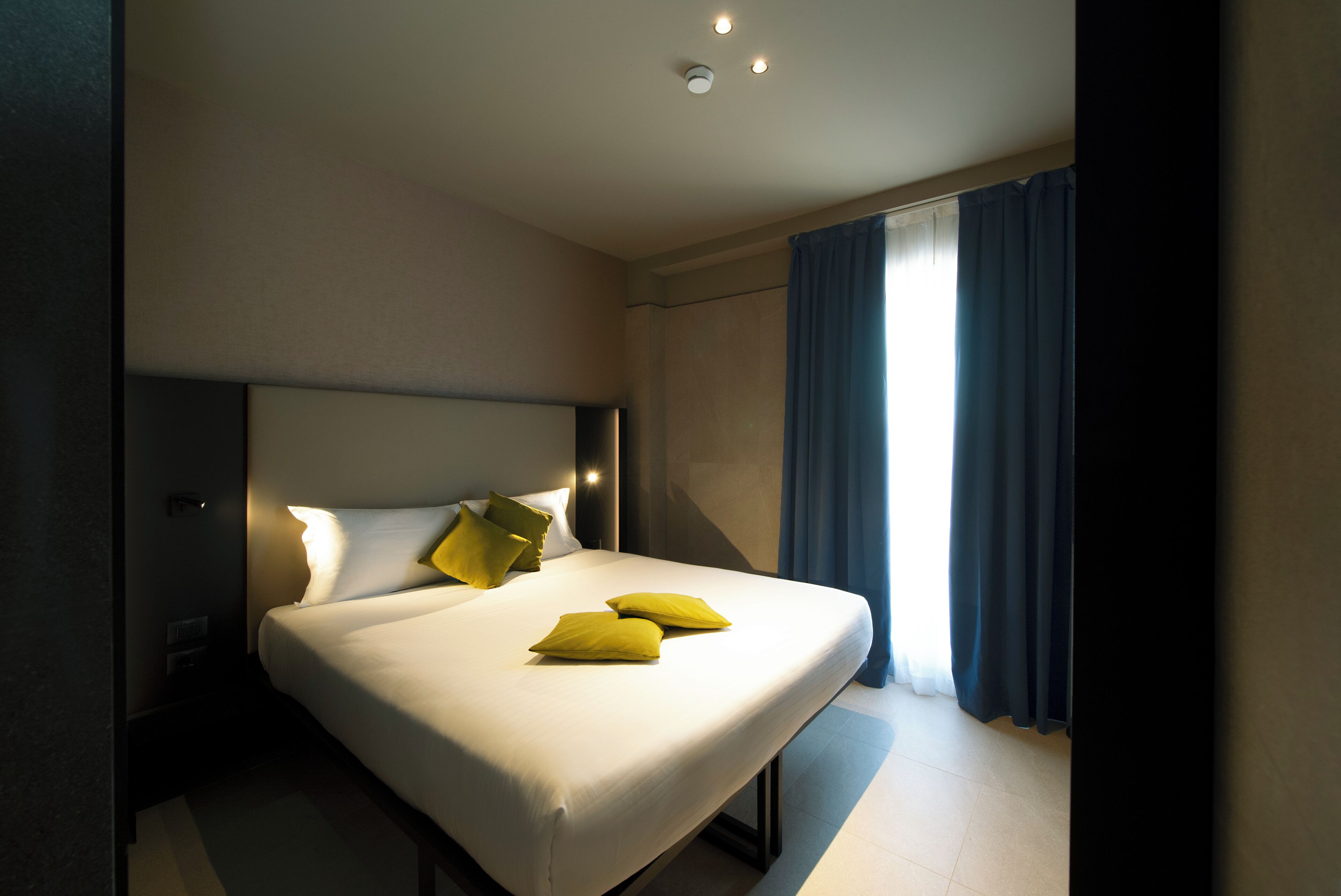 A hotel room with a large bed, a nightstand, and a window with curtains.