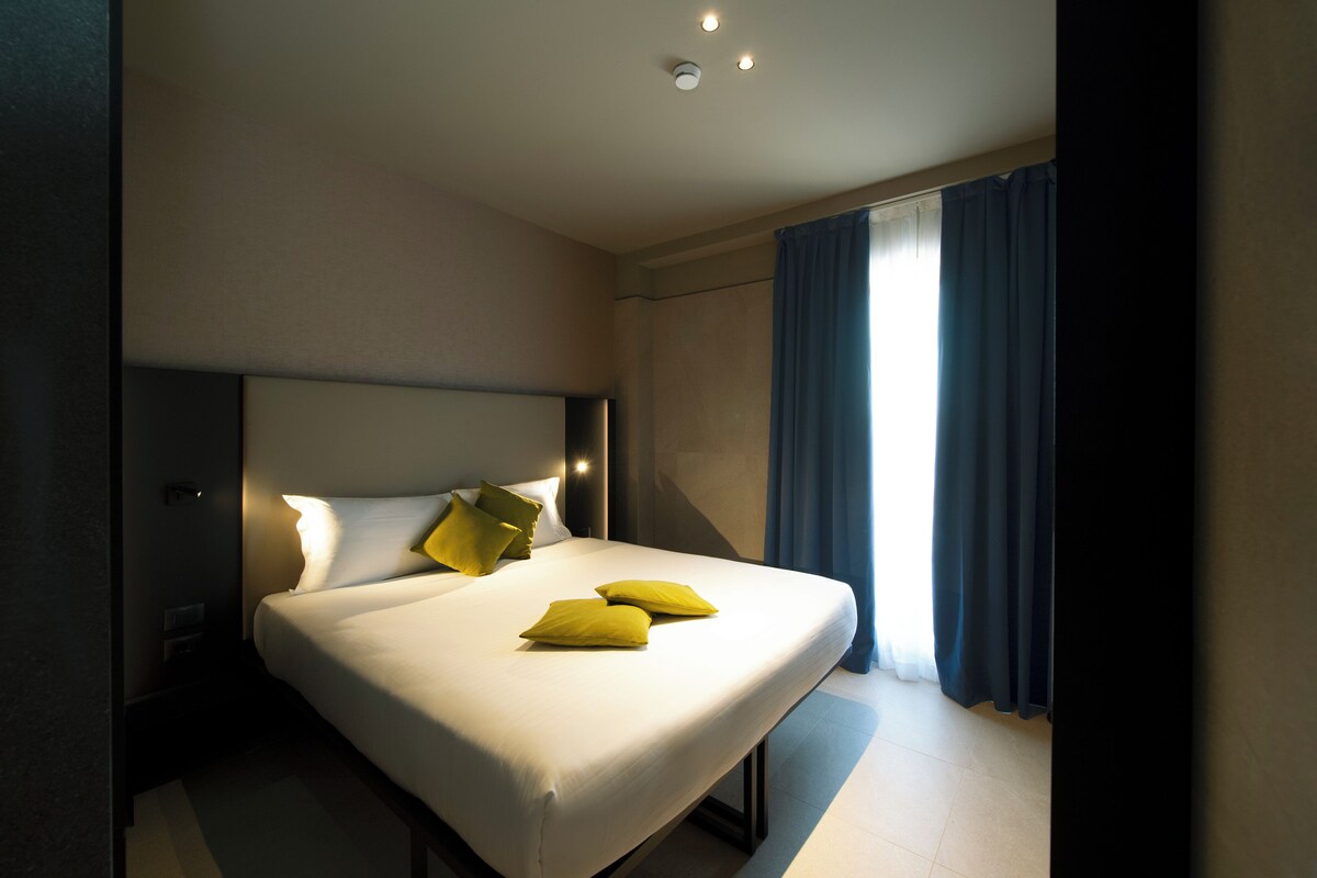 A hotel room with a large bed, a nightstand, and a window with curtains.