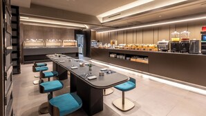 A modern bar area with a long counter, multiple stools, and a variety of beverages and food items. - Scarlatti Hotel Milano (Milan)