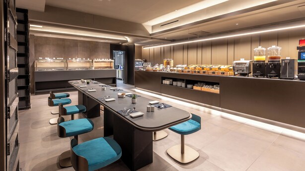 A modern bar area with a long counter, multiple stools, and a variety of beverages and food items. - Scarlatti Hotel Milano (Milan)